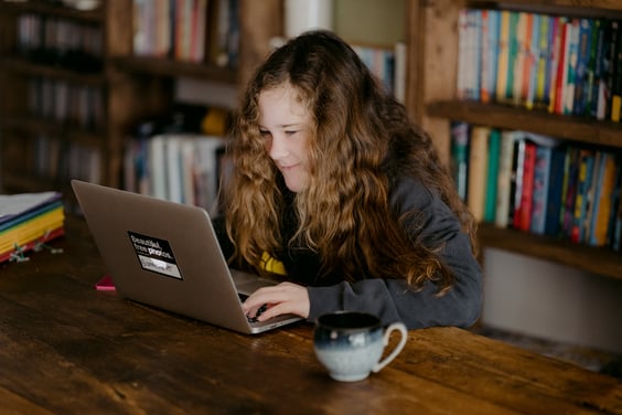 A teenager sits at a table and looks at a laptop screen