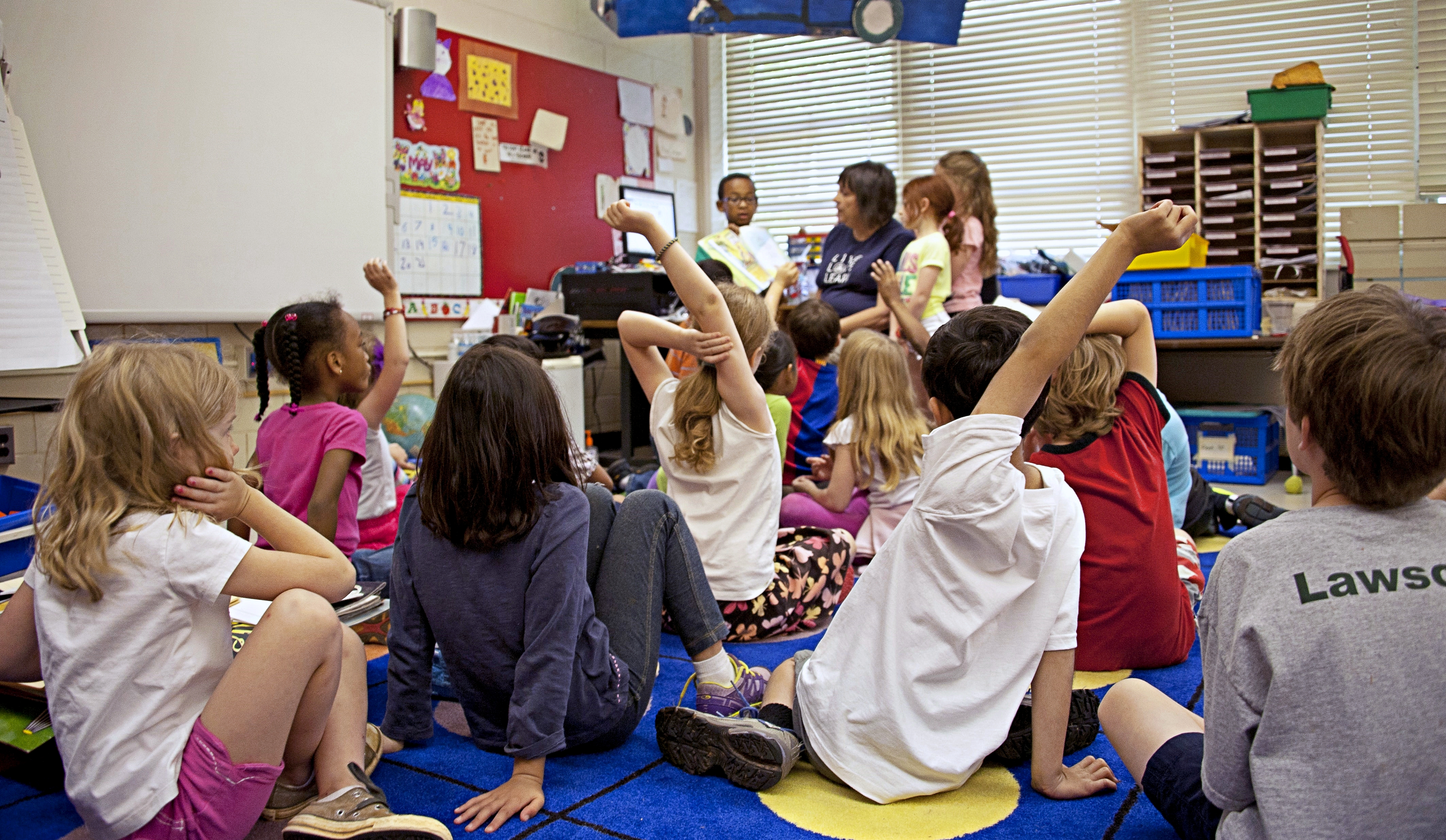 Children sit on the floor in front of a teacher
